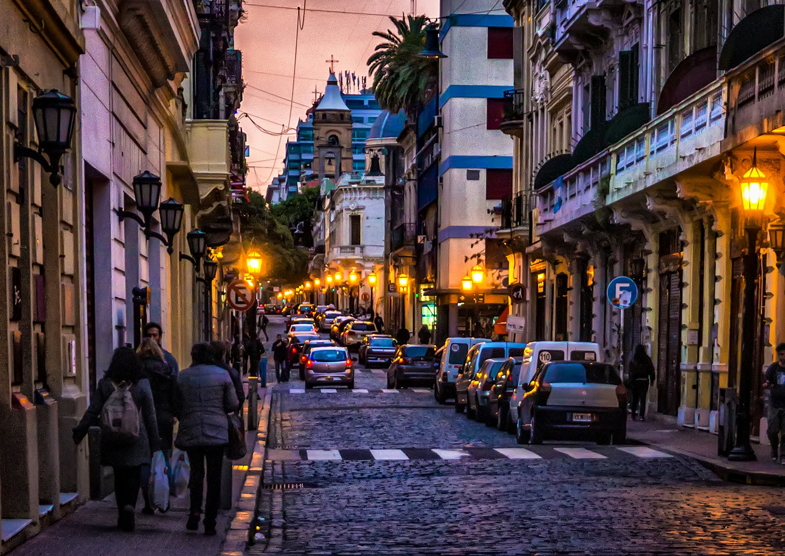 People walk on a sidewalk lining a cobblestone street in Buenos Aires' San Telmo neighborhood at dusk